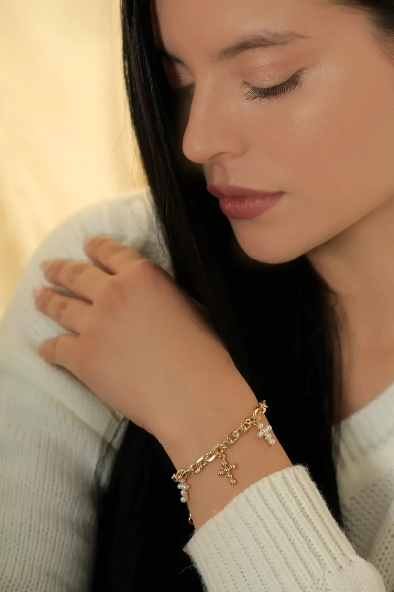 Pulsera dorada con dijes de cruz y perlas en baño de oro 24k. 